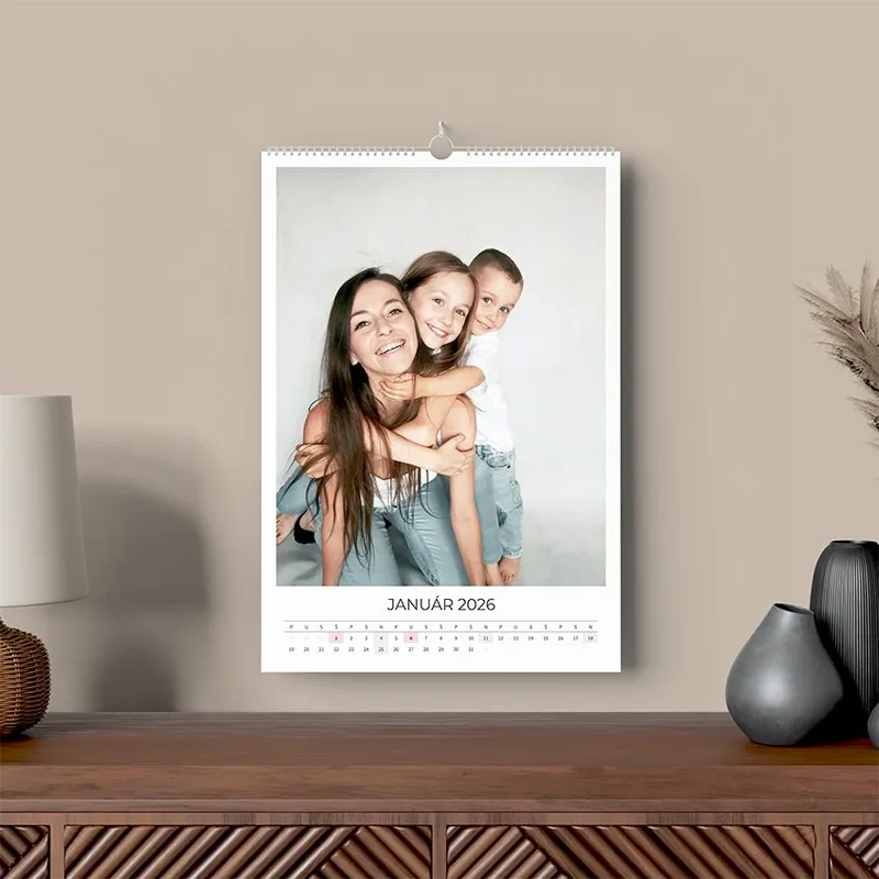 Nástenný fotokalendár formátu A3 zavesený na stene nad drevenou komodou, na liste rodinná fotografia a mesiac január